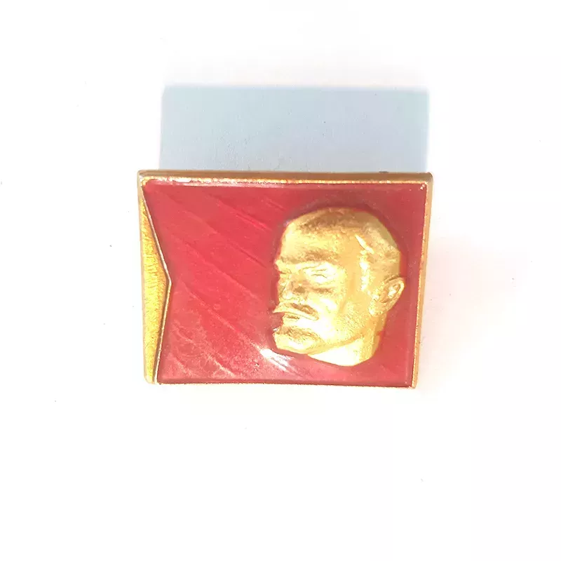 Pin's rectangulaire, orientation paysage, illustré avec la tête de Lénine couleur or et en relief sur un fond rouge.