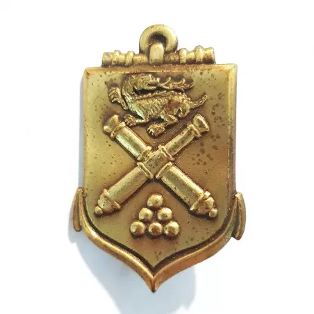 Insigne École d'Application de l'Artillerie, de couleur bronze, en forme d'écu fusionnée à une encre avec symboles en relief.