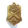 Insigne École d'Application de l'Artillerie, de couleur bronze, en forme d'écu fusionnée à une encre avec symboles en relief.
